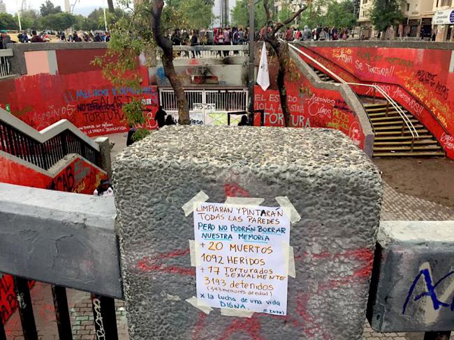“They’ll clean and paint all the walls, but they won’t be able to erase our memory,” reads a sign at a fleeting memorial in Plaza Dignidad, Santiago, Chile. (Manuela Badilla Rajevic)
