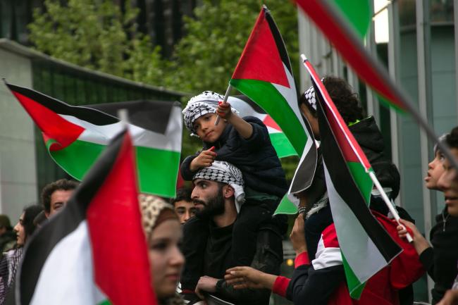 A boy waves a Palestinian flag while he sits atop a man's shoulders. They are wearing keffiyehs at a rally outside of the Israel embassy in Santiago. Protesters called for a ceasefire in Gaza. (Folil Pueller)
