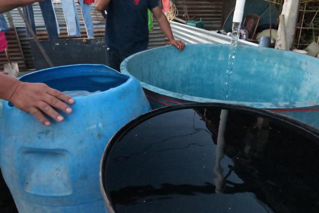 Residentes del asentamiento San Julián en Chinautla reciben su asignación semanal de agua, llenando sus toneles. (Melanie Ford Lemus)