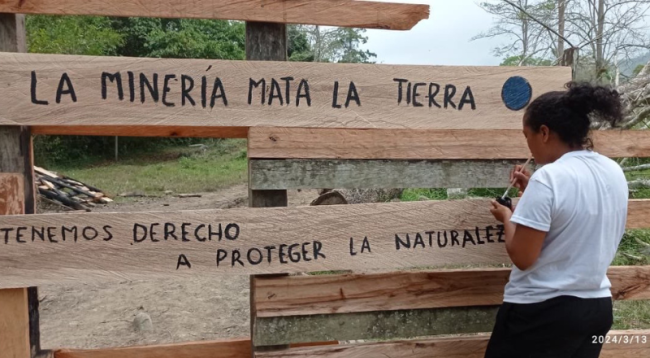 Nalleli Sepúlveda pinta un portón de madera que la Comunidad de Paz reconstruyó después de que fue destruido. (Comunidad de Paz de San José de Apartadó)