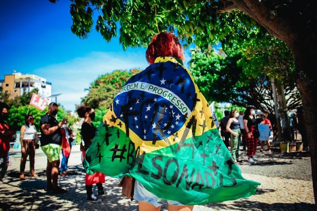 A protester wearing the Brazilian flag painted with "Out Bolsonaro."  On May 29, 2021, hundreds of thousands in over 200 cities joined protests demanding an end to Bolsonaro's presidency. (Mídia NINJA / Flickr / CC BY-NC 2.0)