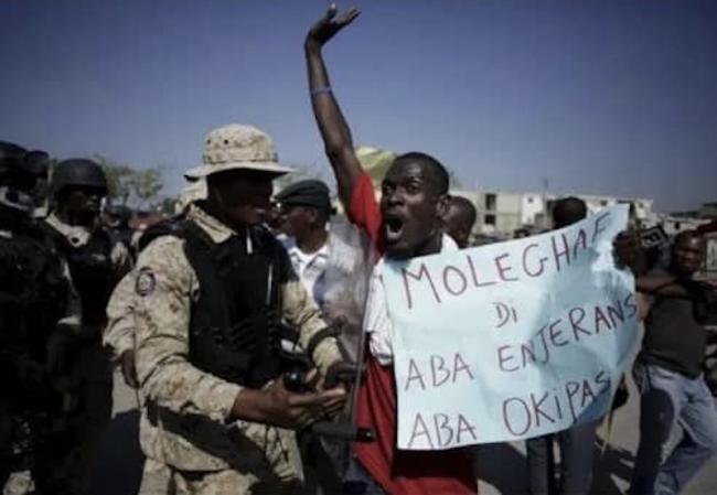 Domini Resain, the mobilization minister of MOLEGHAF, holds a sign that reads “MOLEGHAF Says no to Foreign Meddling and Occupation” at a protest in 2022. MOLEGHAF is the National Movement for Liberty and Equality of Haitians for Fraternity. (MOLEGHAF)