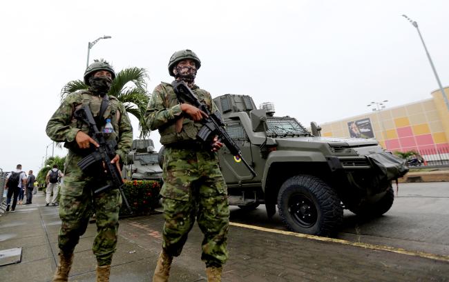 Two armed military soldiers walk alongside tanks. During Noboa’s visit to Los Ríos province, he checked on the status of local military operations. Babahoyo, Ecuador. February 8, 2024. (Carlos Silva / Presidencia de la República / Flickr / PDM 1.0 DEED)
