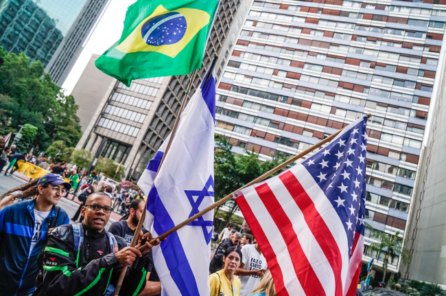 Una persona porta las banderas de Brasil, Israel y Estados Unidos durante una manifestación en apoyo a Bolsonaro de cara a las elecciones de 2018, en São Paulo, 9 de septiembre de 2018. (PABLO ALBARENGA / MÍDIA NINJA / CC BY-NC 4.0)