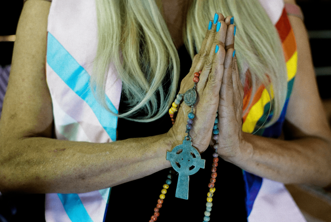 Jaque Chanel clasps her hands around rainbow-colored rosary beads. Chanel—who is wearing a stole with the transgender flag on one side and the rainbow pride flag on the other–founded the first church for trans people in Brazil. (Felipe Avila)
