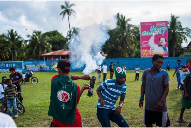 Miskitu youth at the Yatama Grand Finale celebration with fireworks with Daniel Ortega (FSLN) billboard behind them.  (Photo by Alex McDougall)