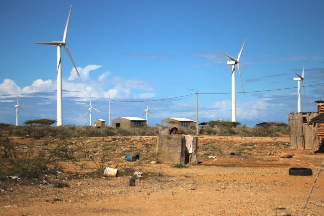 A girl from the Aerutkajui community brushes her teeth in a roofless bathroom, Jepírachi wind turbines appear in the background. Despite the wind farm benefits, some families don't have running water or adequate housing. (Photo by Christina Noriega)