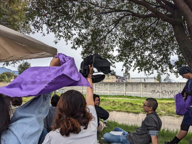 Attendees at a community lecture wave to people imprisoned at Buen Pastor prison. In the distance, cell bars can be seen covered in colorful towels, blankets, and clothing belonging to incarcerated women. October 13, 2023. (Joseph Hiller)