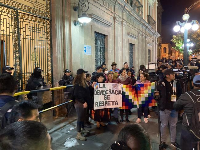 Arce supporters gather outside the gates of Palacio Quemado with a wiphala flag on Wednesday evening after the president's address. (Benjamin Swift)