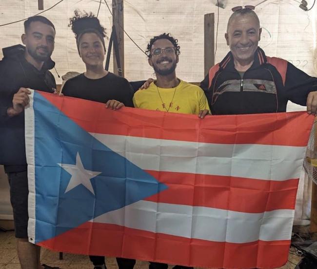 Libre Sankara (in yellow) holds the Puerto Rican flag along with Bisan Owda, a Palestinian journalist, and two other Palestinians. (Libre Sankara)