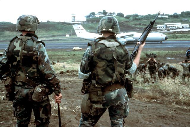 U.S. soldiers carrying M16A1 rifles watch an aircraft arrive in Grenada as part of Operation Urgent Fury, the U.S. invasion, November 3, 1983. (TSGT MIKE CREEN / Wikimedia Commons / Public domain)