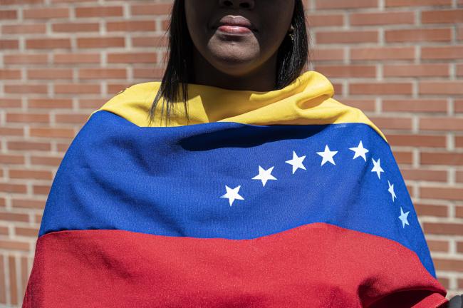 A woman covered with a Venezuelan flag waits for opposition leader María Corina Machado near a polling station in Los Chorros in eastern Caracas on July 28, 2024. (Marcelo Pérez del Carpio)