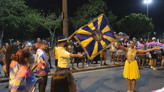 The master of ceremony and standard-bearer hold up Paraíso do Tuiuti’s peacock blue and gold flag during a Carnival rehearsal in Rio de Janeiro on February 10, 2025. (Constance Malleret)