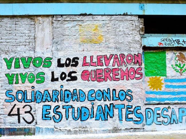 A commemorative mural reads, “Vivos los llevaron Vivos los queremos Solidaridad con los 43 estudiantes desparecidos (“Alive they took them. Alive we want them. Solidarity with the 43 disappeared students”). (Sortica/Wikimedia Commons/CC BY-SA 4.0)