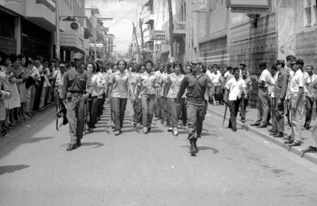 Guerrilla women march down Calle El Conde, Santo Domingo, April 1965. The dark-skinned Black woman marching in the front line (center) is Agustina Rivas, aka Tina Bazuca. (Fondo Milvio Pérez, Archivo General de la Nación, Dominican Republic)