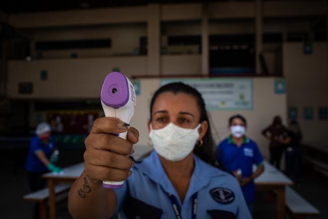 An employee at the State Full-Time School Professor Jacimar da Silva Gama, in Manaus, Amazonas, Brazil, takes the temperature of students arriving for class in September 2020. (IMF/Raphael Alves)