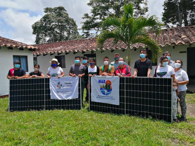 Community members pose with solar panels and the banners of Ríos Vivos movement and the Latin American Movement of People Affected by Dams. ( Archivo Comunidades SETAA)