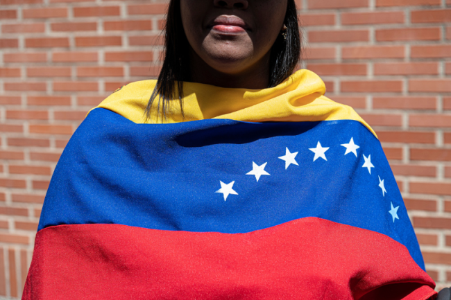 A woman covered with a Venezuelan flag waits for opposition leader María Corina Machado near a polling station in Los Chorros in eastern Caracas on July 28, 2024. (Marcelo Pérez del Carpio)